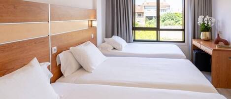 A hotel room with two beds, a wooden headboard, a desk with a vase of flowers, and a window with curtains.
