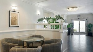 Un hall d’entrée avec un espace salon aux motifs à carreaux, une table en verre, un tableau encadré au mur et une vue sur l’extérieur à travers l’embrasure de la porte.