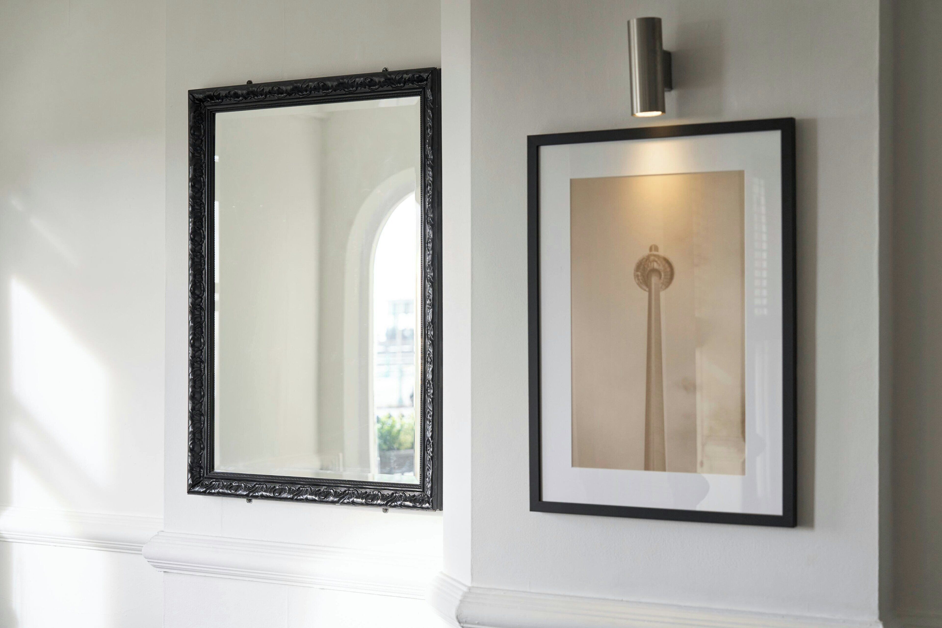 Twee ingelijste kunstwerken aan een muur, één met een zwarte, versierde lijst en de ander met een eenvoudige zwarte lijst.