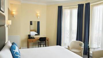 A hotel room with a bed, a desk, a chair, a small table, and a window with curtains.