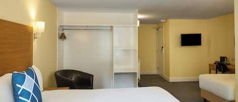 Una habitación de hotel con cama, una silla, escritorio, televisor y armario.