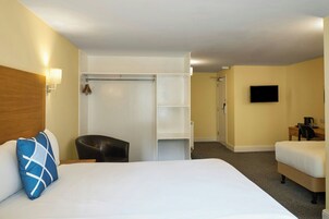 Una habitación de hotel con cama, una silla, escritorio, televisor y armario.