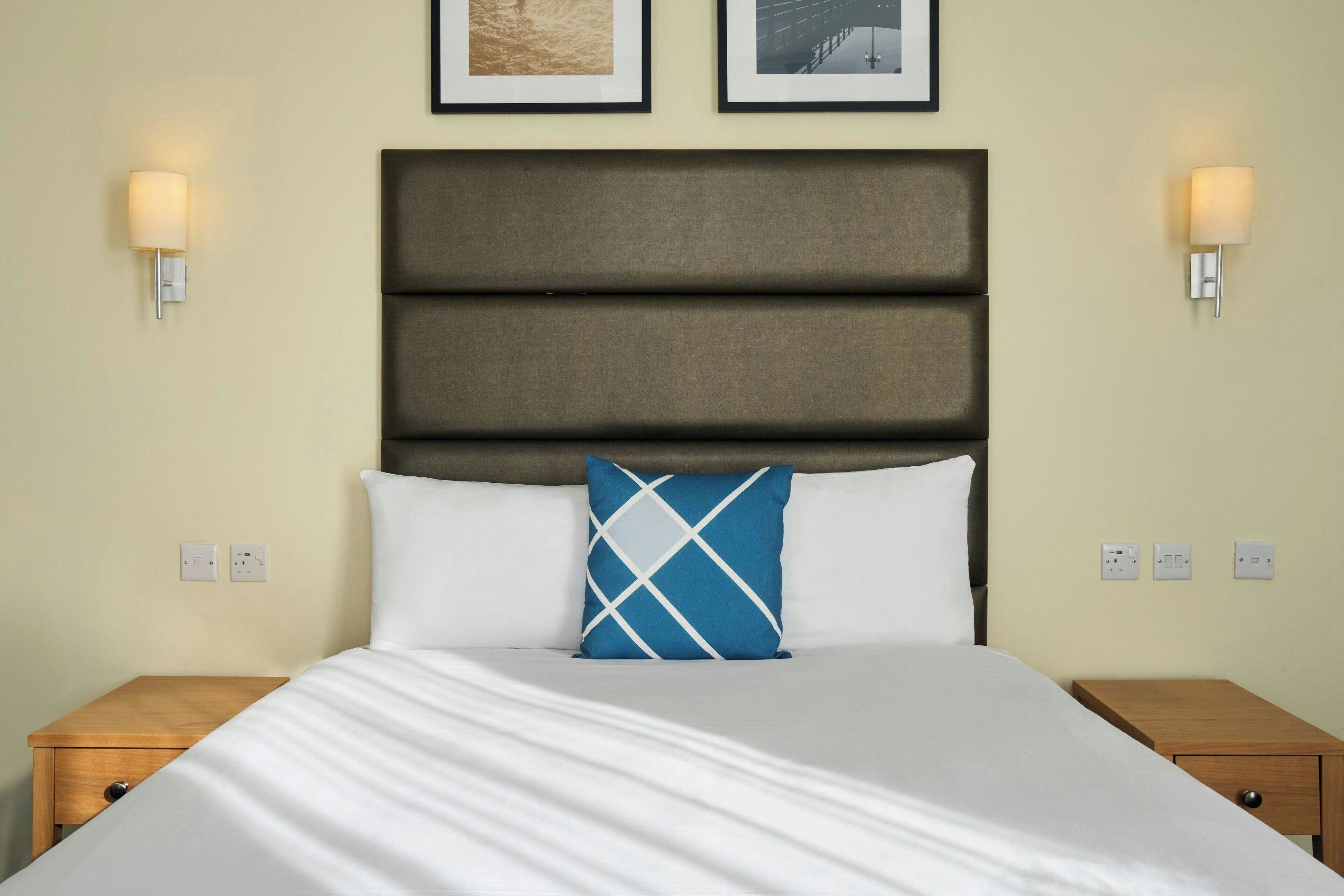 A neatly made bed with a blue and white pillow, two bedside tables, and wall-mounted light fixtures.