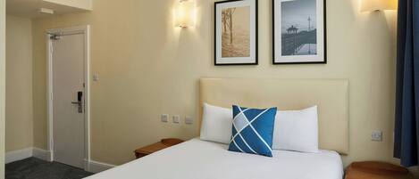 A hotel room with a bed, a nightstand, a door, and two wall-mounted light fixtures.