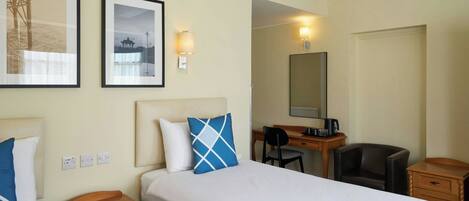 Quarto de hotel com uma cama grande, duas mesas de cabeceira, uma escrivaninha com cadeira, um espelho e duas molduras com quadros na parede.