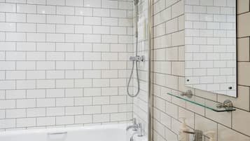 Un baño moderno con azulejos blancos tipo metro, mampara de vidrio, bañera blanca y espejo con repisa de vidrio encima.