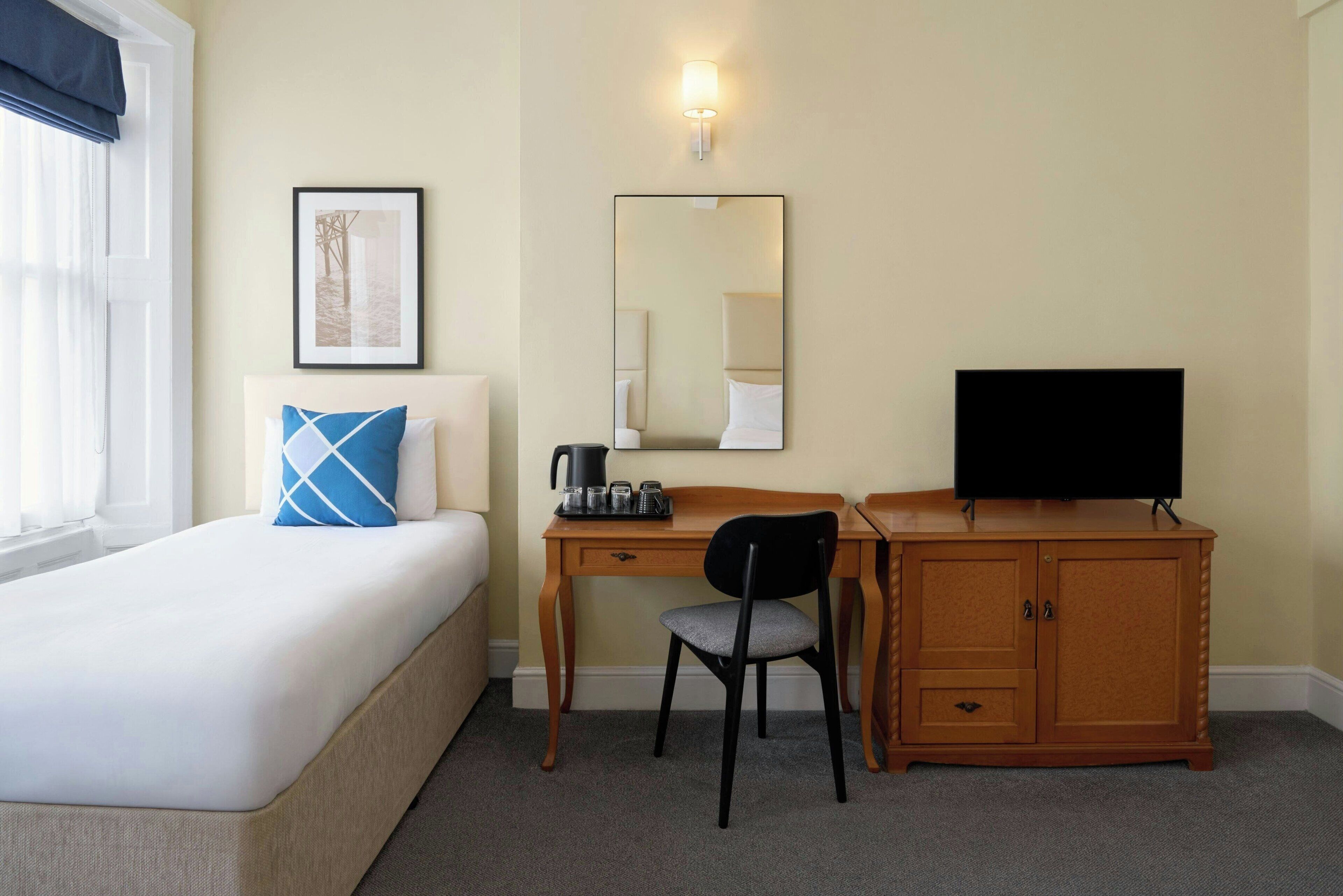 Une chambre d’hôtel avec un lit, un bureau, une chaise, une télévision, un miroir et un tableau au mur.