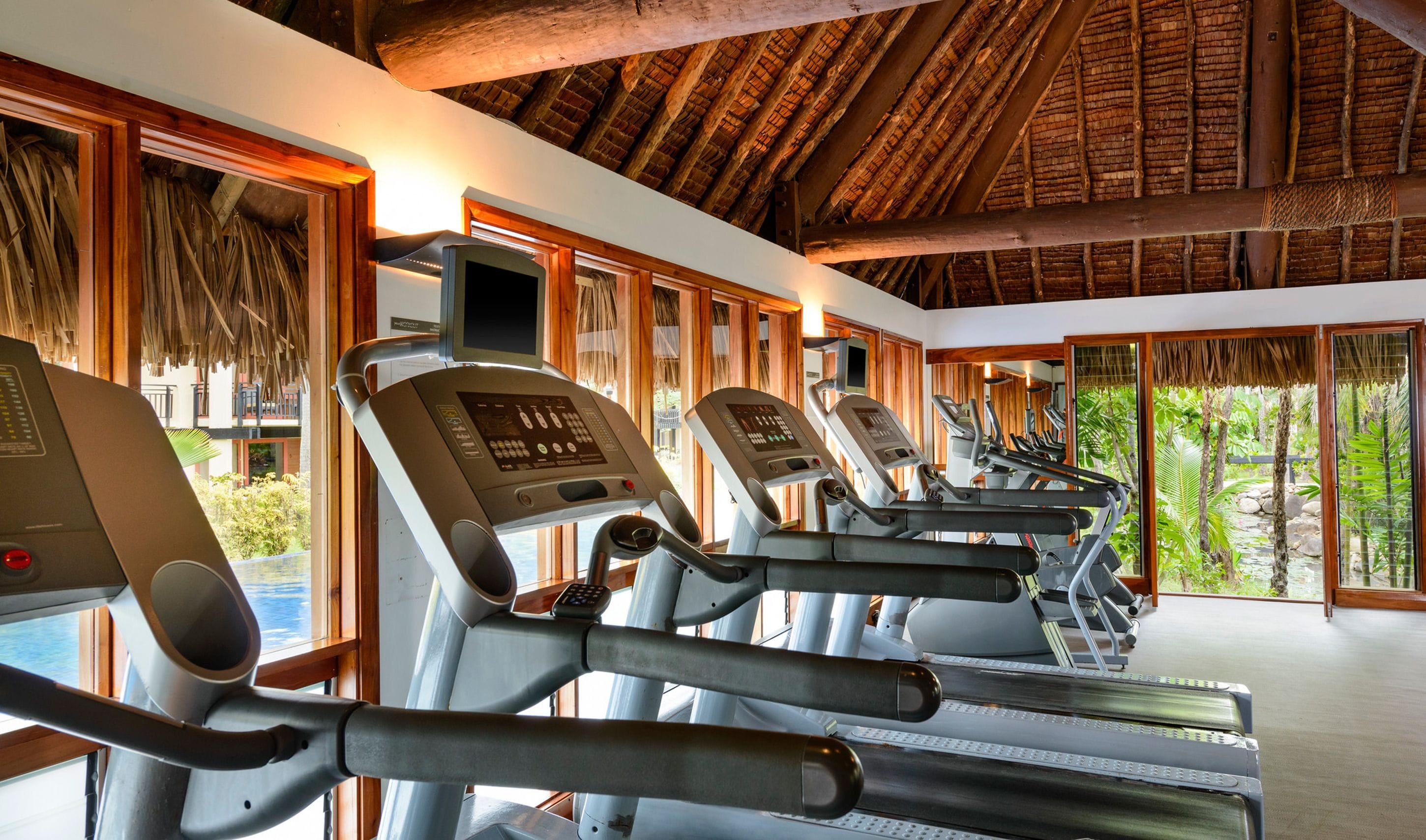 A fitness center with treadmills, large windows, and a thatched roof.