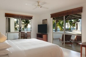 A hotel room with a bed, a TV, a ceiling fan, and a balcony with a view of palm trees and the ocean. - Sheraton Denarau Villas (Nadi)