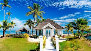 A beachfront property with a white gazebo, a pathway leading to a door, and palm trees.