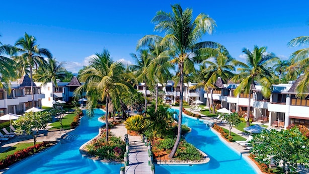 A resort with a central swimming pool, palm trees, and multiple guest rooms.