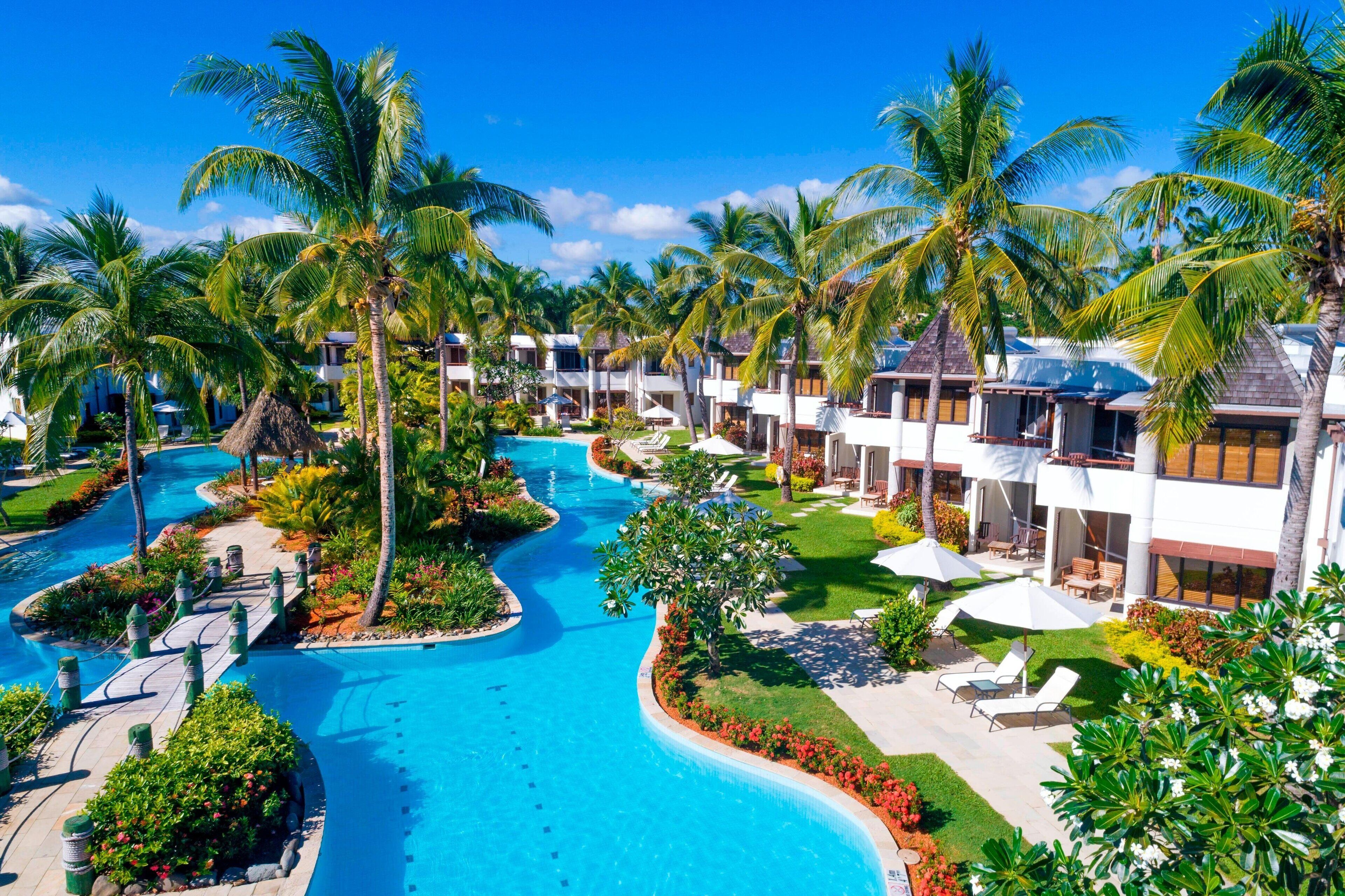 Un resort con piscina central, palmeras y varias villas para huéspedes.