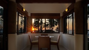 A dining area with a round table and wicker chairs, large windows with a view of palm trees and sunset, and a modern architectural design.