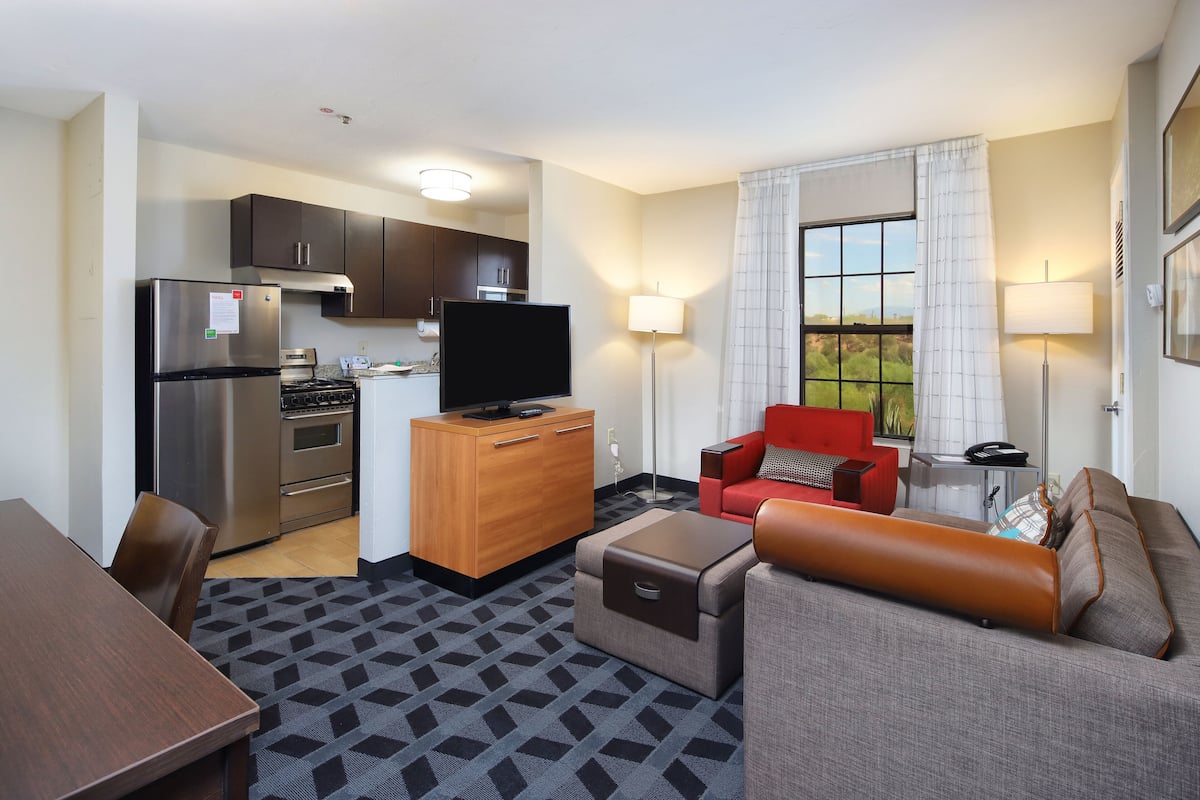 A compact hotel room with a kitchenette, a flat-screen TV, a sofa, and a dining area.