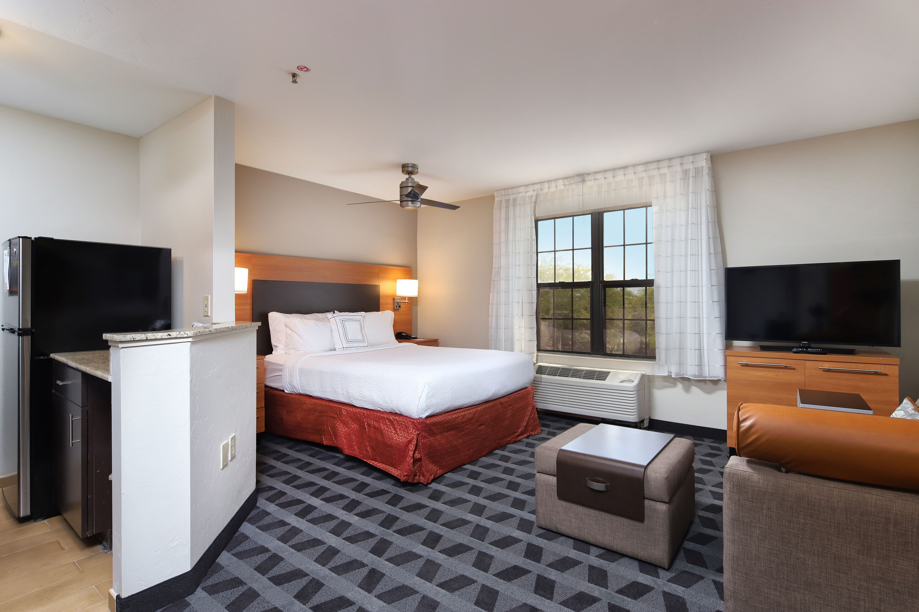 A hotel room with a bed, a desk, a television, a ceiling fan, and a window with curtains.