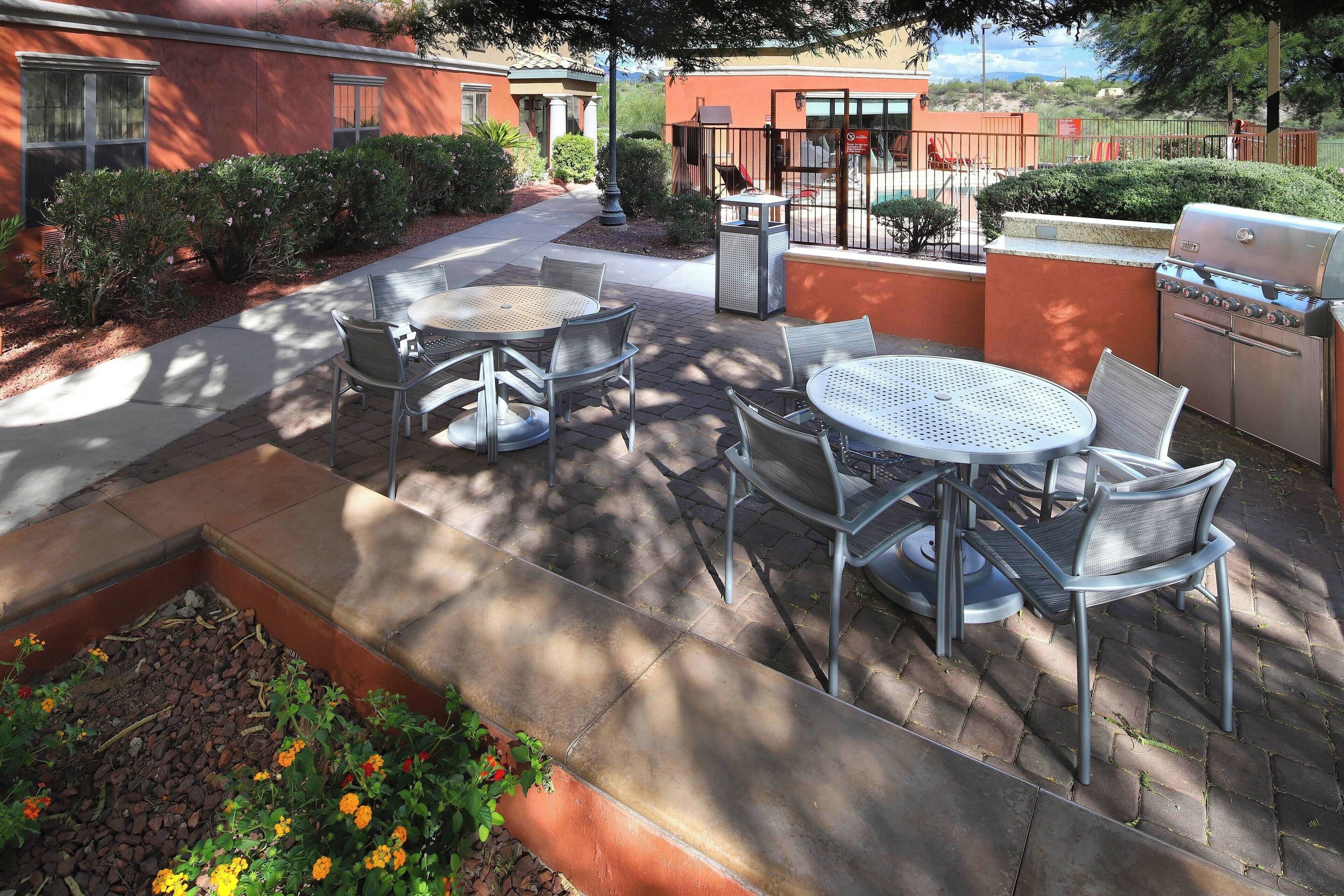 An outdoor patio with a grill, seating area, and a pathway leading to a building.