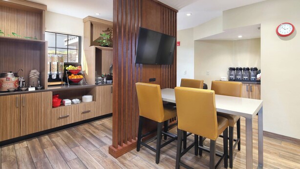 A modern kitchen with wooden cabinets, a central island with a sink, and a dining area with yellow chairs. - TownePlace Suites by Marriott Tucson (Tucson)