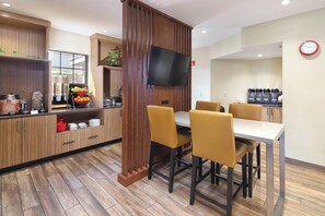 A modern kitchen with wooden cabinets, a central island with a sink, and a dining area with yellow chairs.