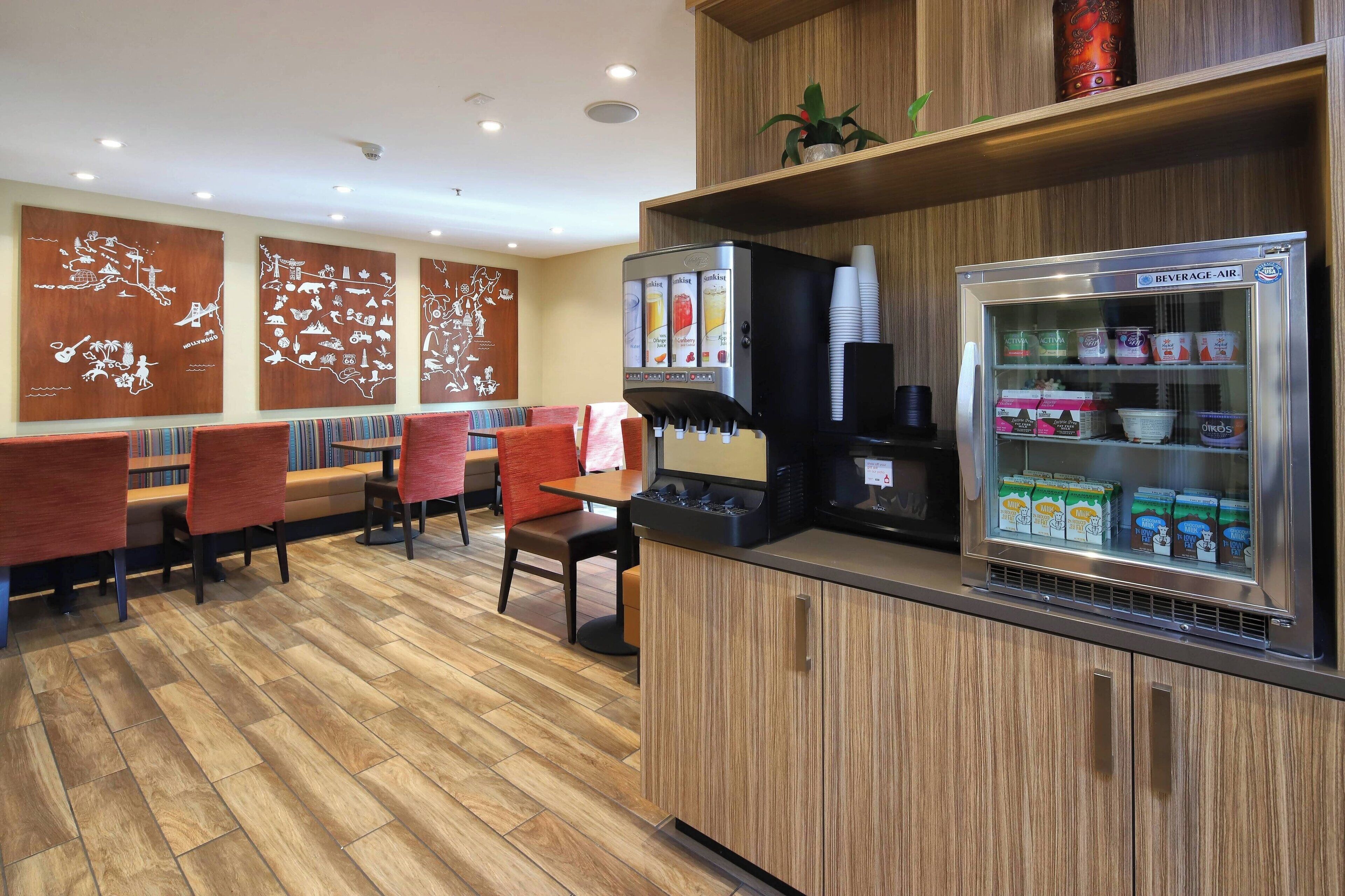 Un restaurant doté d’un plancher en bois, de chaises rouges, d’un distributeur de boissons et d’un réfrigérateur rempli de produits alimentaires.