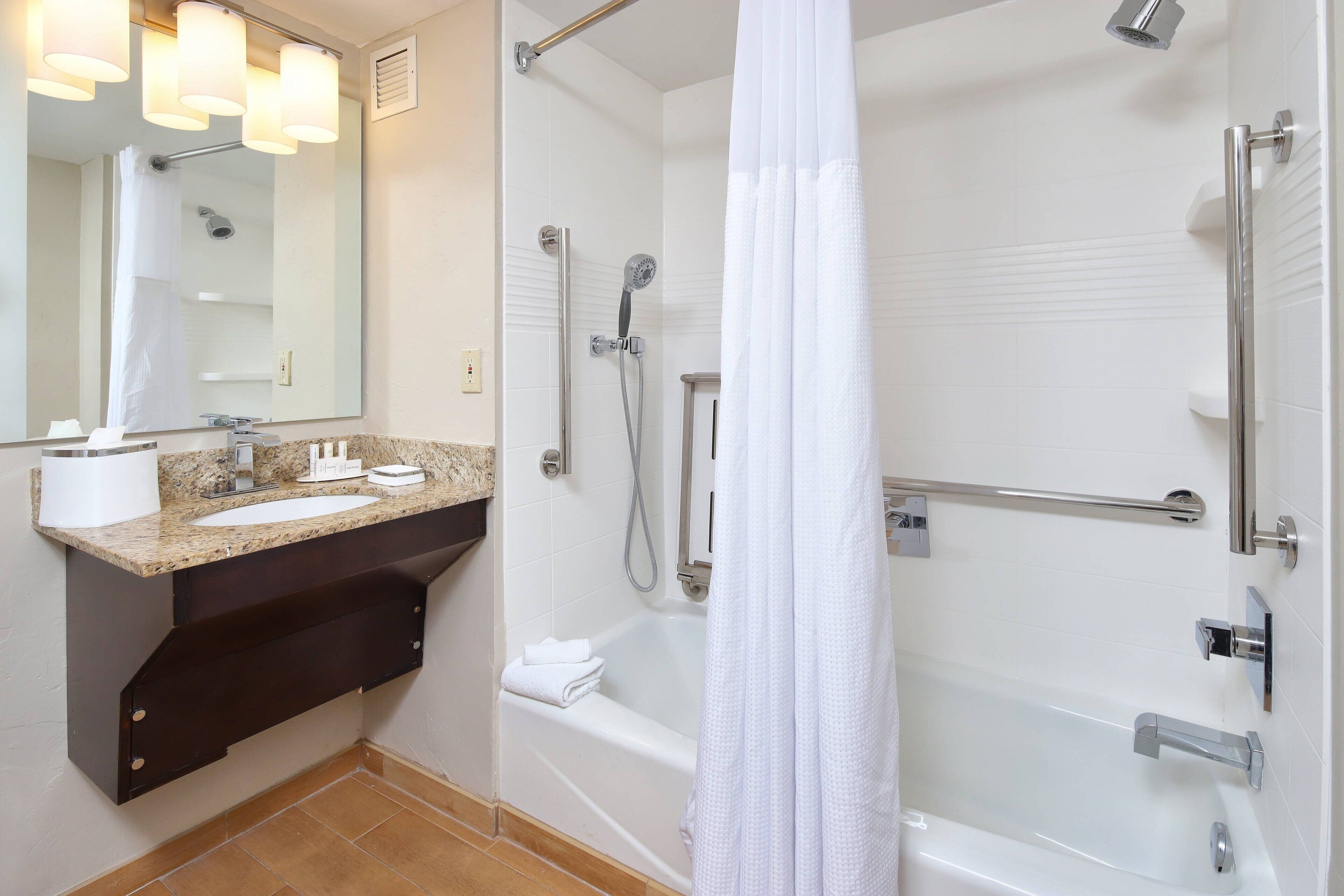 A modern bathroom with a granite countertop sink, a large mirror, a shower with a handheld showerhead, and a bathtub.