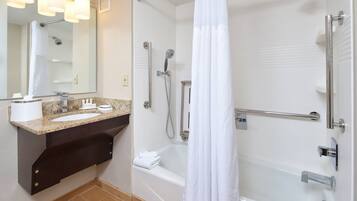 A modern bathroom with a granite countertop sink, a large mirror, a shower with a handheld showerhead, and a bathtub.