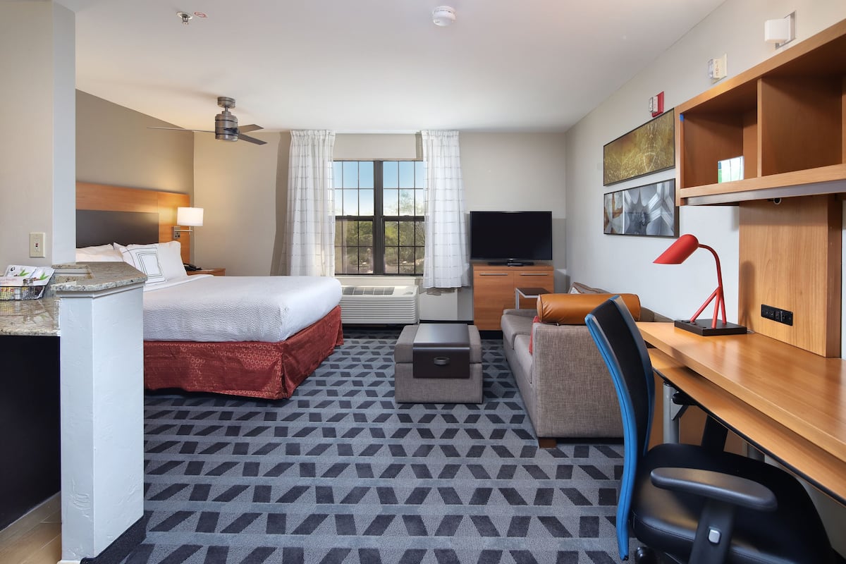 A hotel room with a bed, desk, chair, and a view of the outdoors.