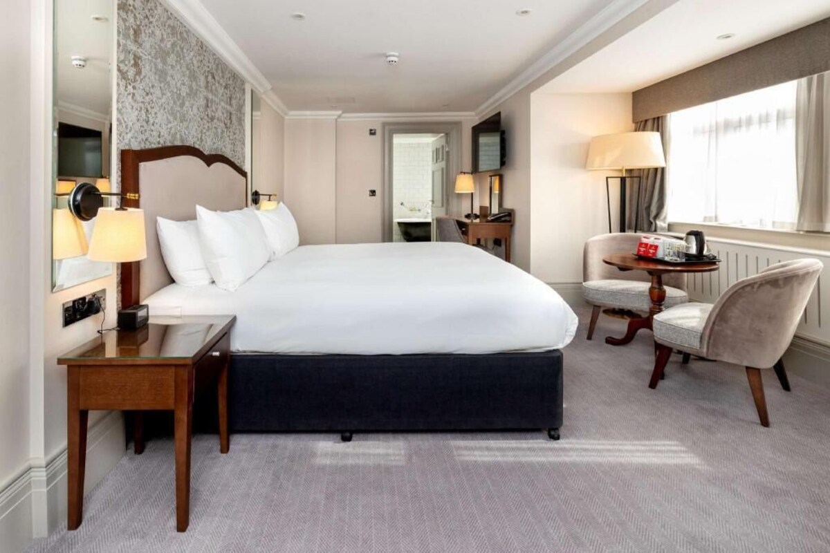 A hotel room with a large bed, a desk, a chair, a TV, and a window with curtains.
