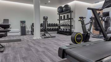 A modern gym with cardio equipment, weightlifting stations, and neatly arranged dumbbells.