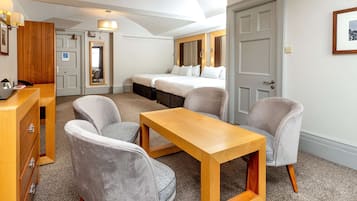 Habitació d'hotel amb un llit, dues butaques, una taula de fusta, escriptori amb calaixos, un mirall i una porta.