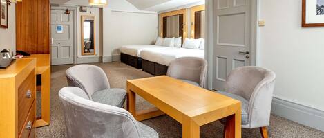 Habitación de hotel con cama, dos sillones, una mesa de madera, un escritorio con cajones, un espejo y una puerta.