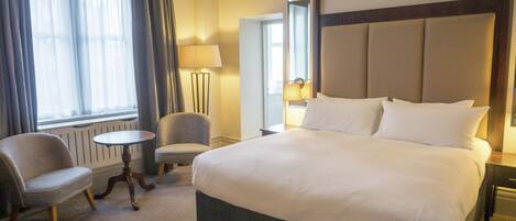 A hotel room with a large bed, two armchairs, a small table, and a window with curtains.