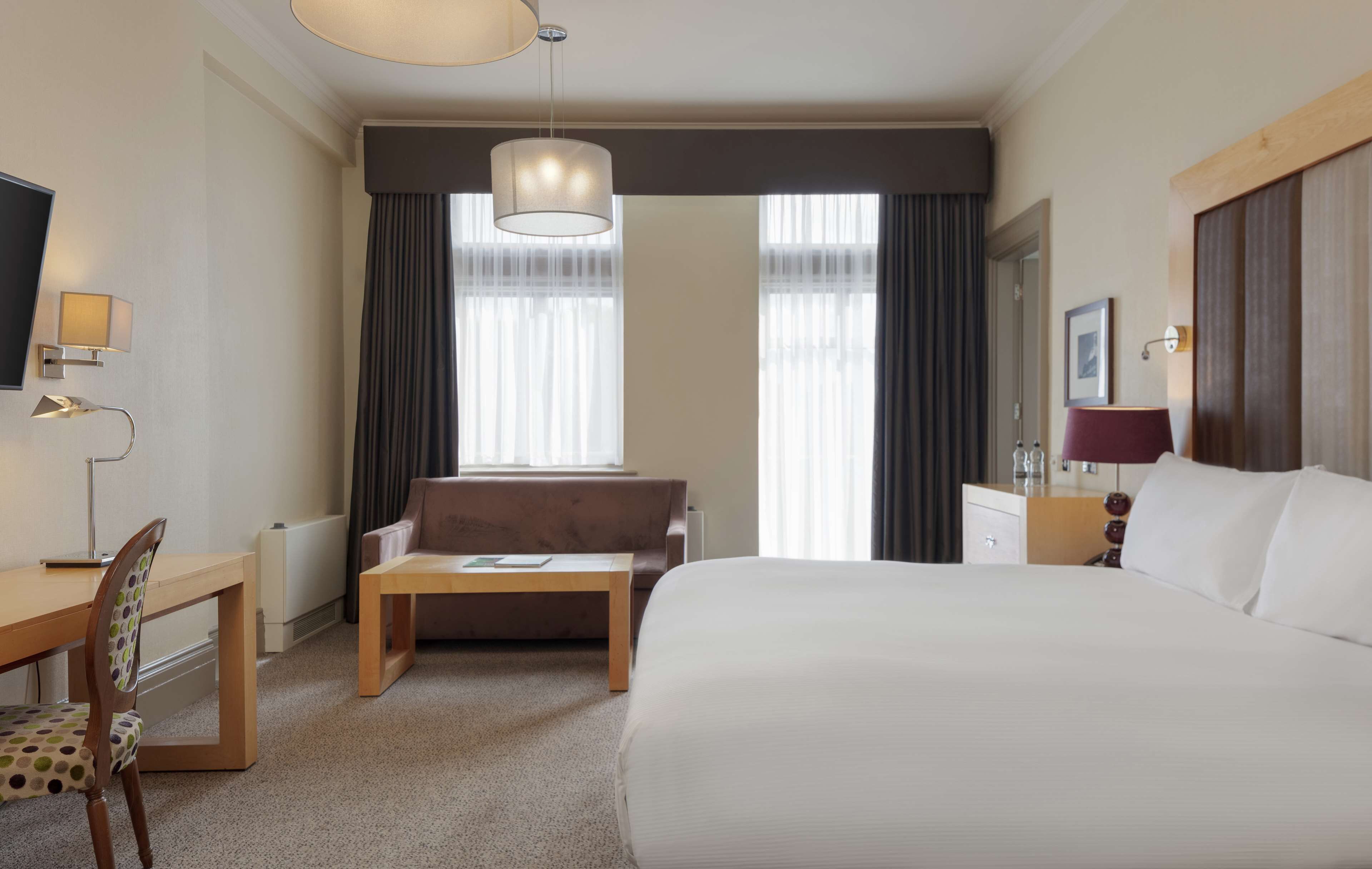 A hotel room with a large bed, a desk with a chair, a sofa, a coffee table, and a TV.