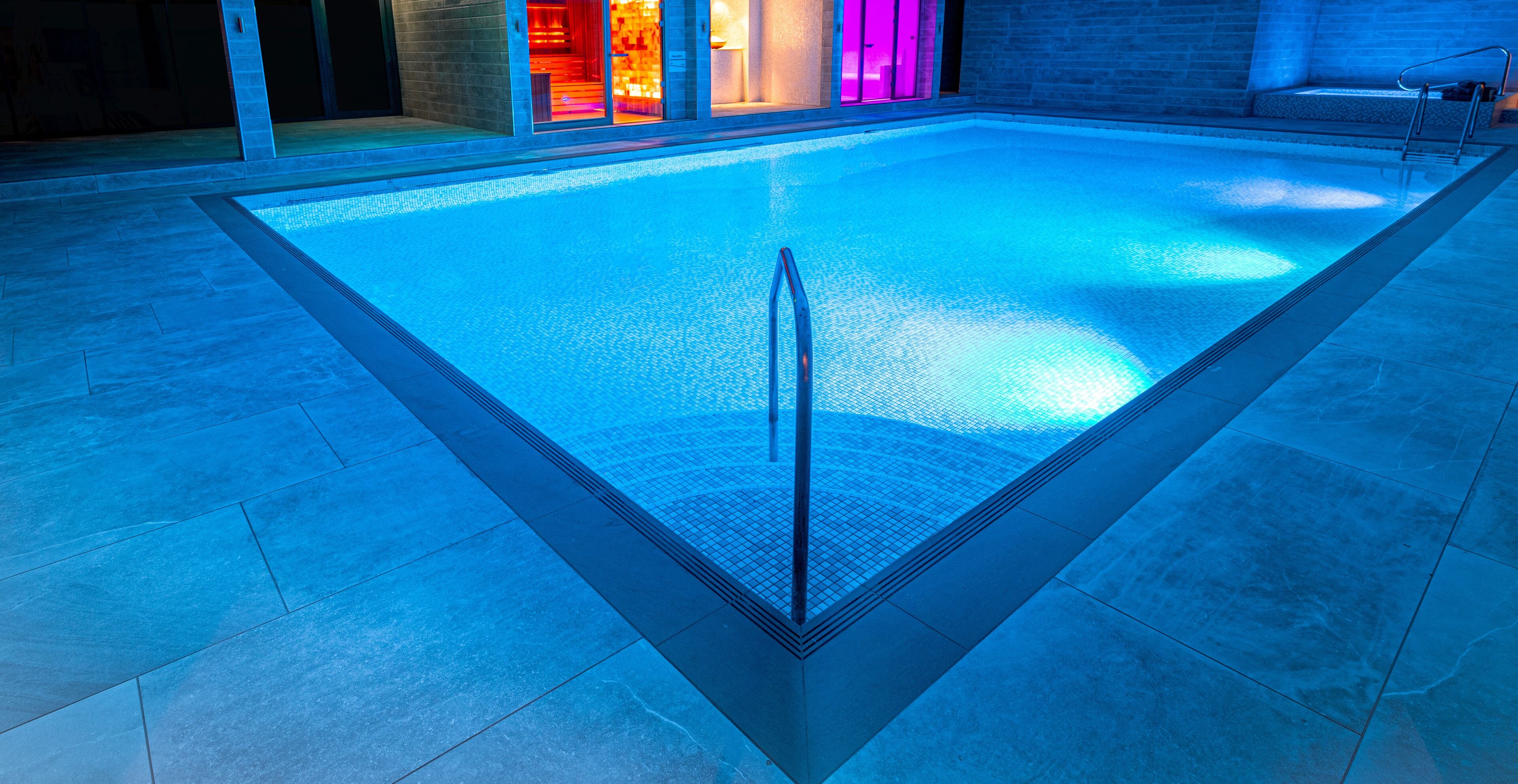 A swimming pool with a clear water line, a single ladder, and a tiled floor.