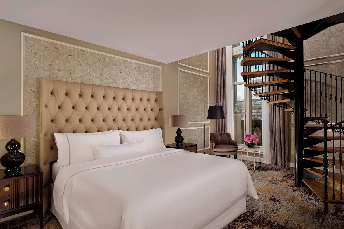 Un dormitorio espacioso con una cama grande, una escalera de madera y vistas al exterior.