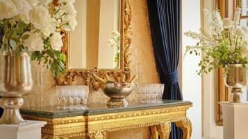 A luxurious room with a gold-framed mirror, a marble table with a gold decorative border, and a vase of white flowers.