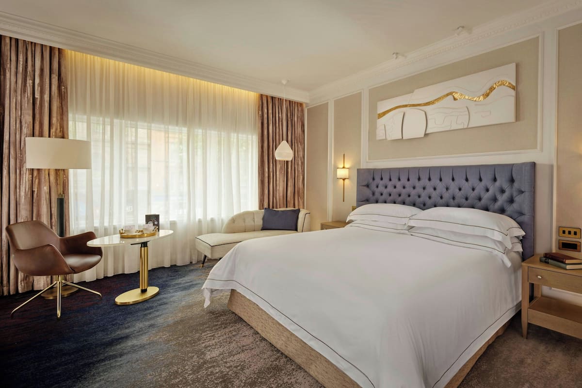 Una habitación de hotel con una cama grande, una mesa redonda, una silla y una lámpara.
