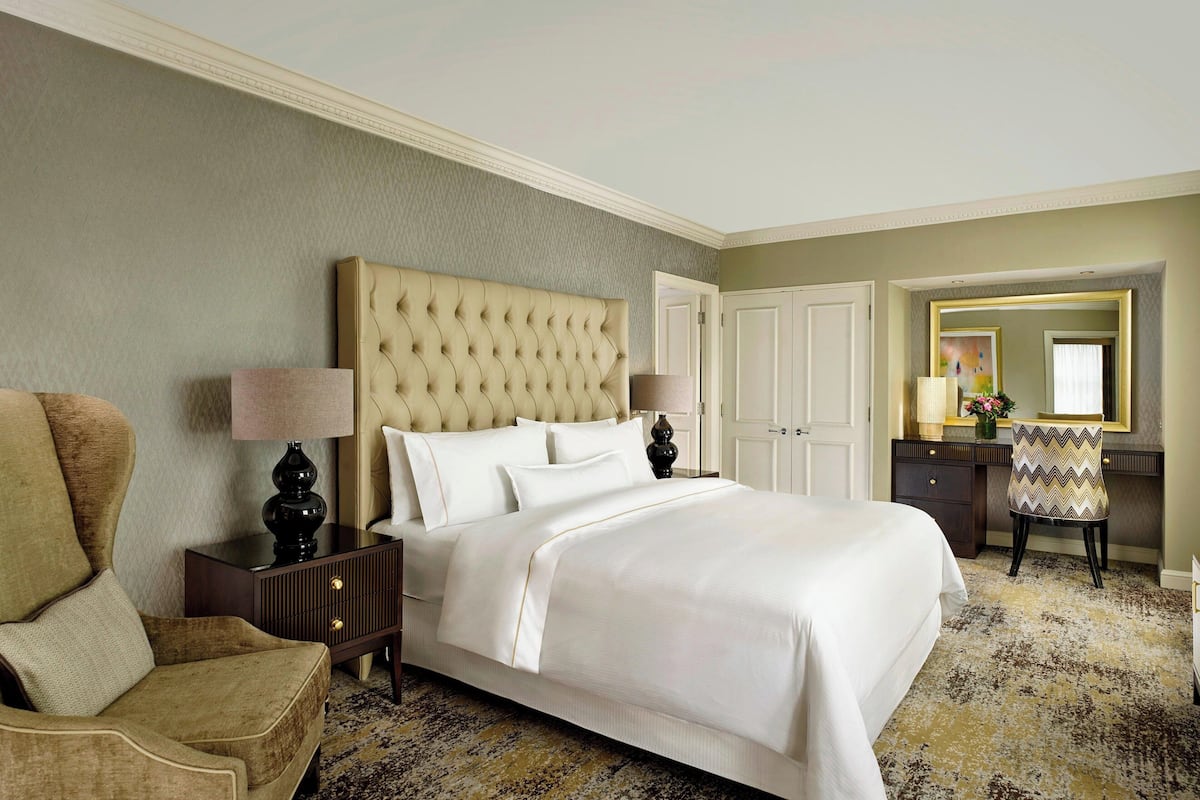 Una habitación de hotel con una cama grande, una silla, un tocador y un espejo.