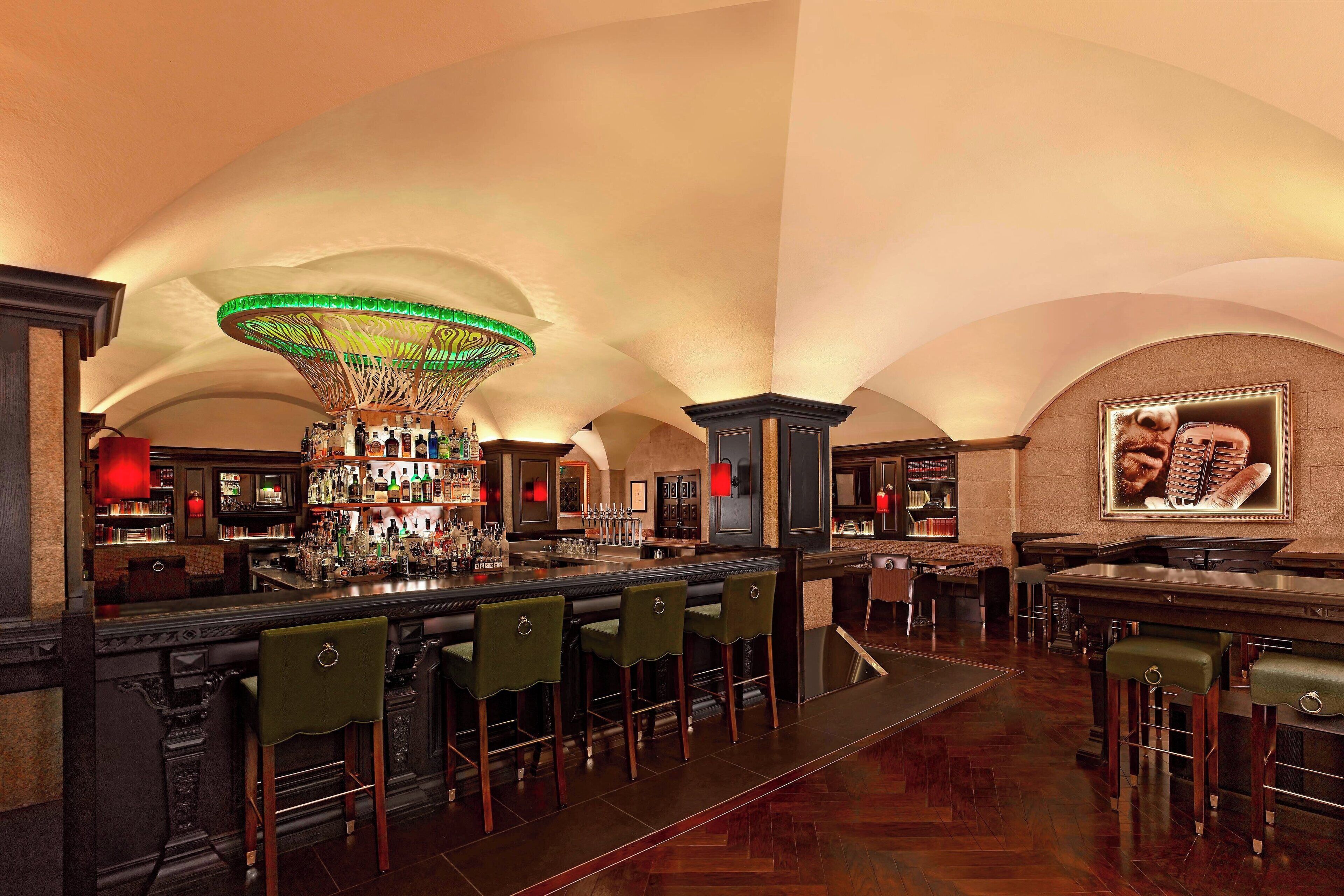 Zona de bar con techos altos, una lámpara central y varios taburetes.