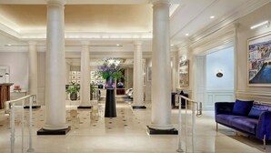 A spacious lobby with high ceilings, large columns, a central floral arrangement, and a blue sofa. - The College Green Hotel Dublin, Autograph Collection (Dublin)