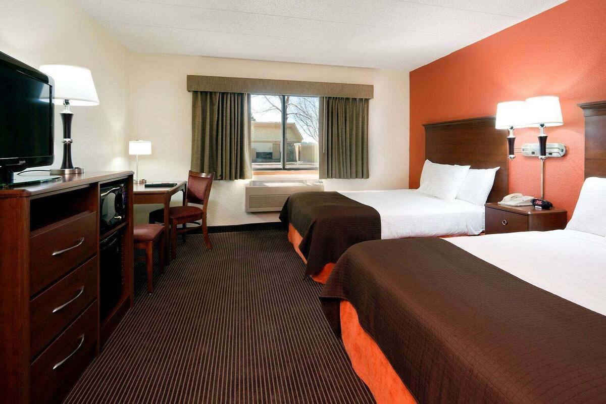 Een hotelkamer met twee bedden, een bureau met stoel, een televisie en een raam met gordijnen.