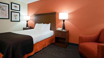 A hotel room with a bed, two bedside tables with lamps, a chair, and framed artwork on the wall.