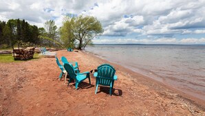 A beach with turquoise chairs and a pile of logs. - AmericInn by Wyndham Ashland (Ashland)
