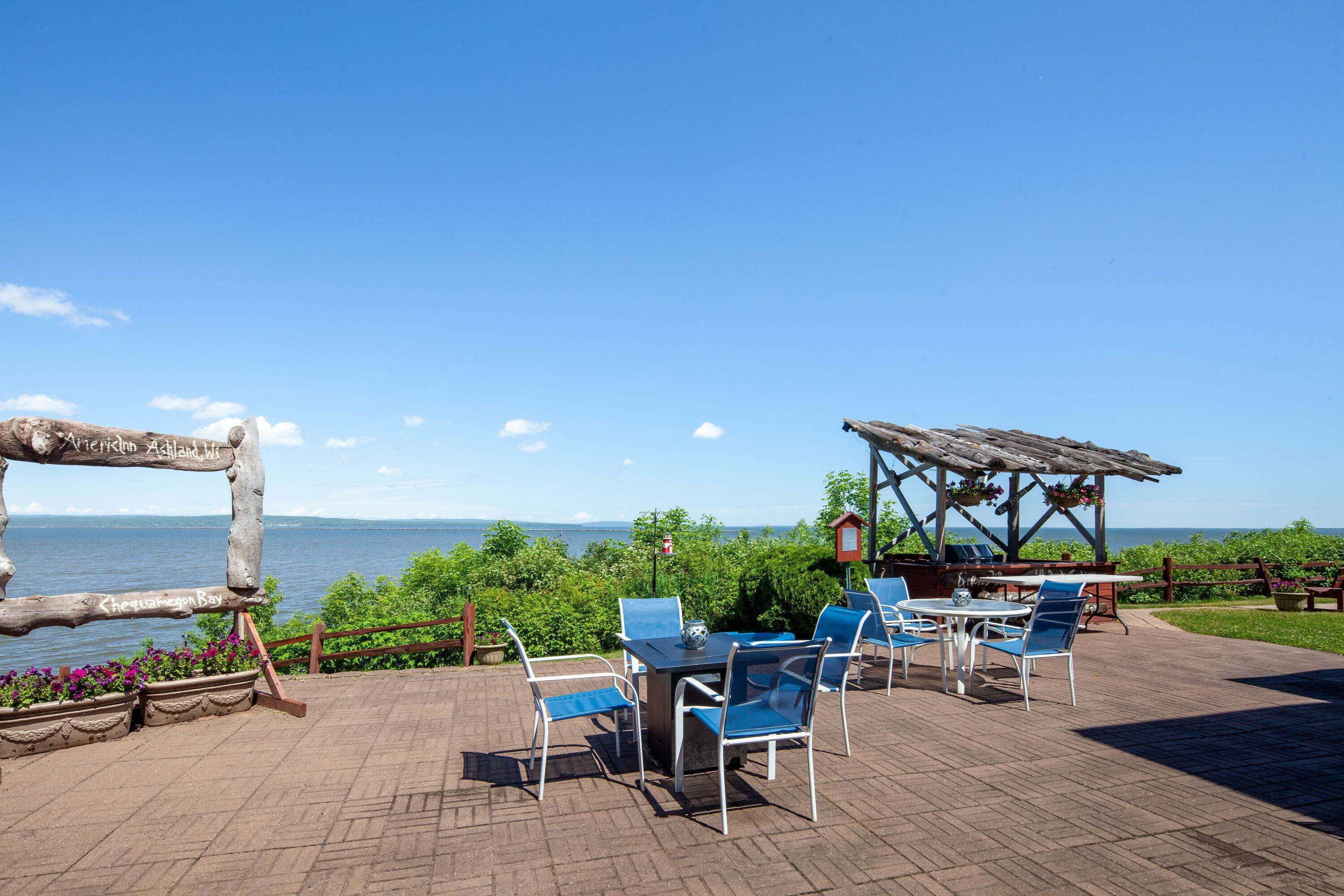 An outdoor patio with a table and chairs, a wooden pergola, and a view of the sea.