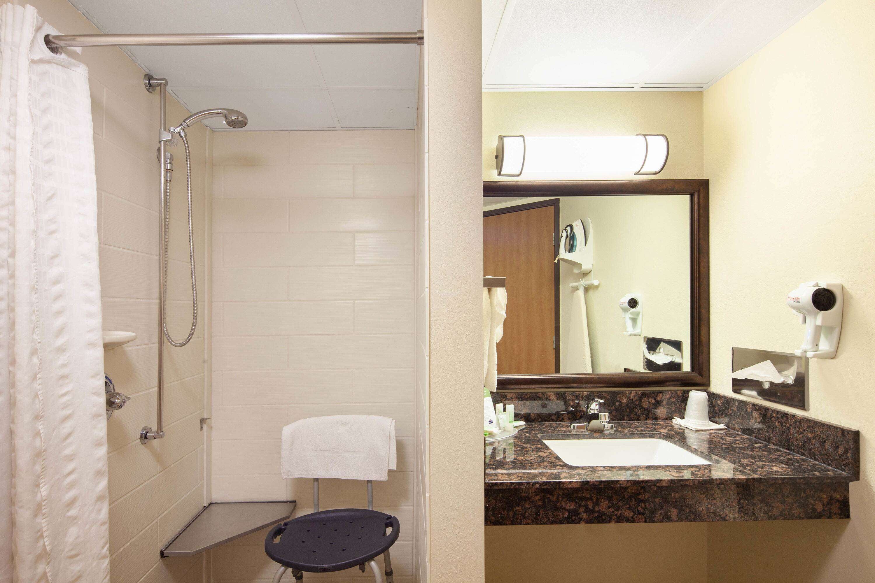 A bathroom with a shower, a sink, a mirror, and a towel rack.