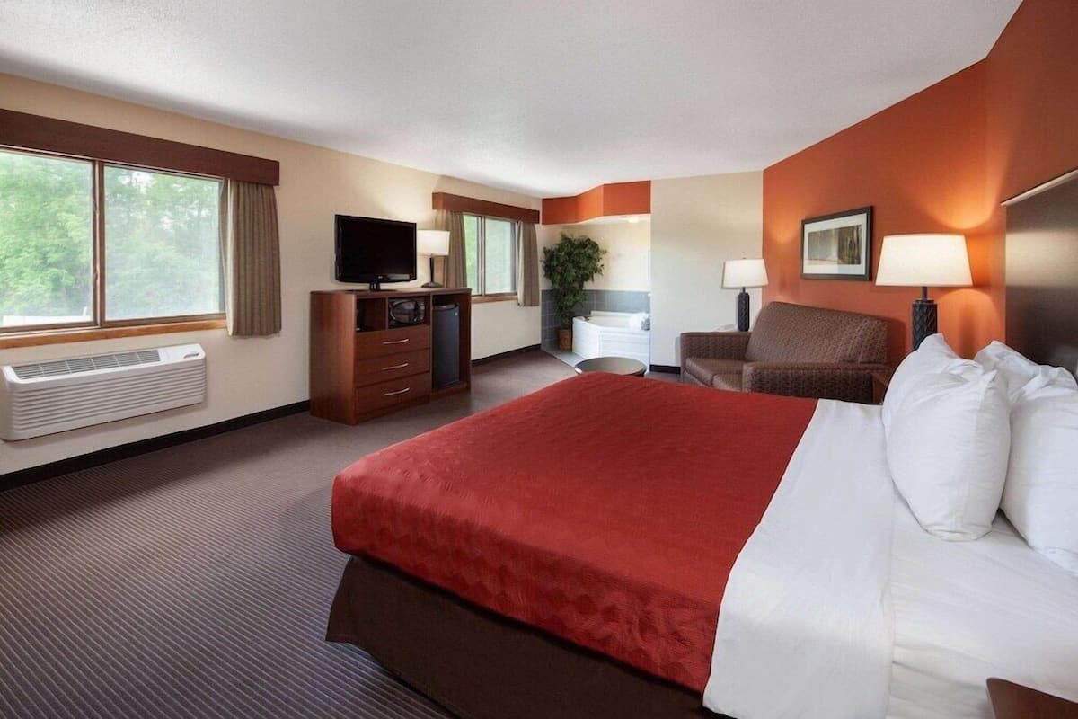 Hotelkamer met een groot bed, een bureau met computer, een stoel, een televisie en een raam met gordijnen.