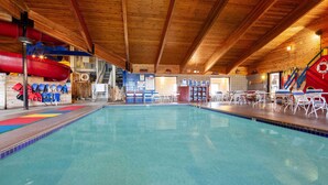 An indoor swimming pool with a wooden ceiling, slides, and poolside chairs. - AmericInn by Wyndham Ashland (Ashland)