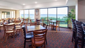 A dining area with multiple tables and chairs, large windows offering a view of the sea, and a carpeted floor. - AmericInn by Wyndham Ashland (Ashland)