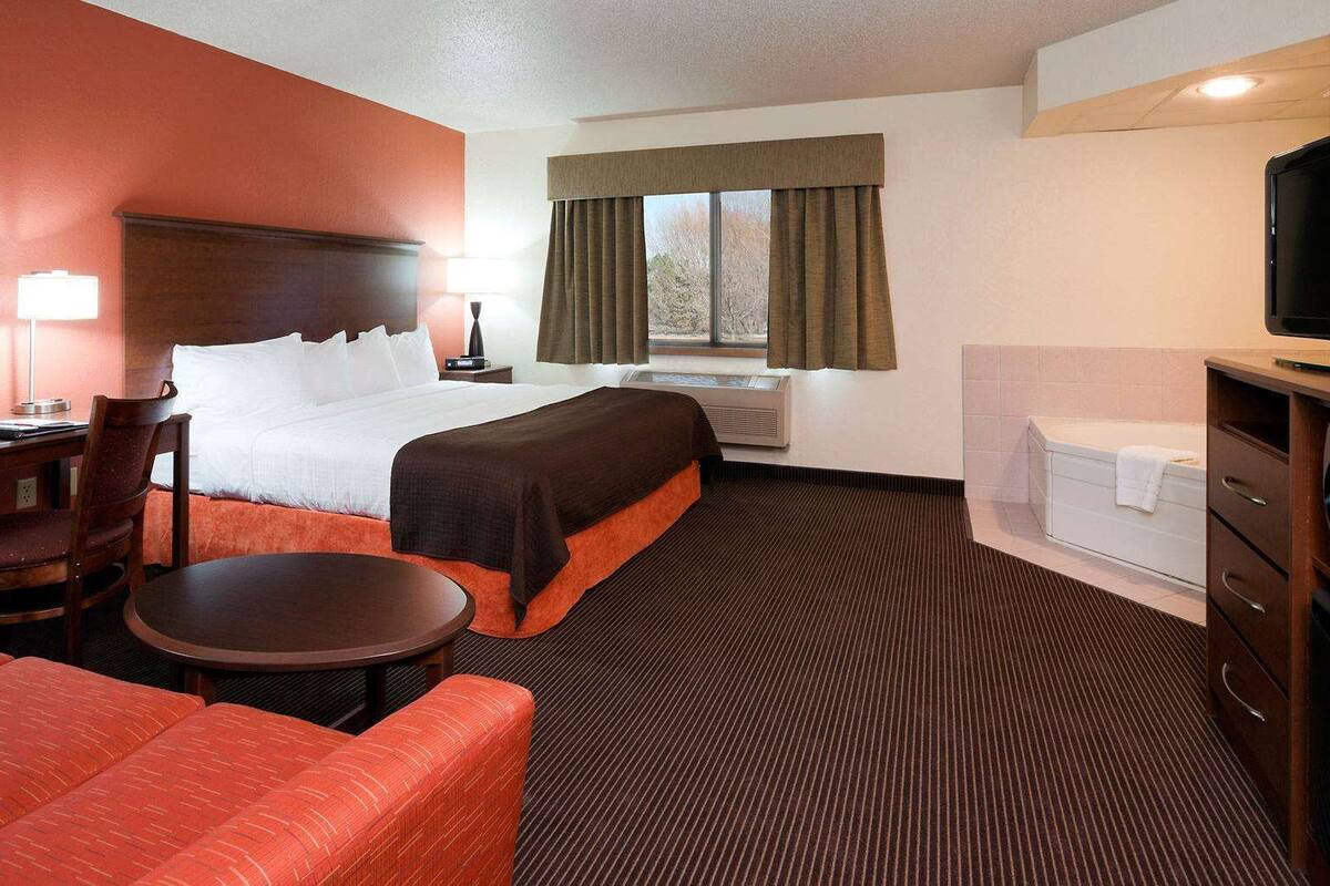 Ein Hotelzimmer mit Bett, Schreibtisch, Stuhl, Fernseher und einem Fenster mit Vorhängen.