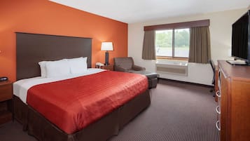 Een hotelkamer met een groot bed, een bureau, een stoel, een televisie en een raam met gordijnen.