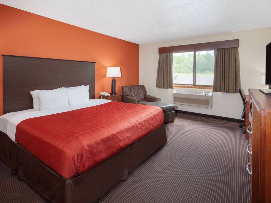 Een hotelkamer met een groot bed, een bureau, een stoel, een televisie en een raam met gordijnen.